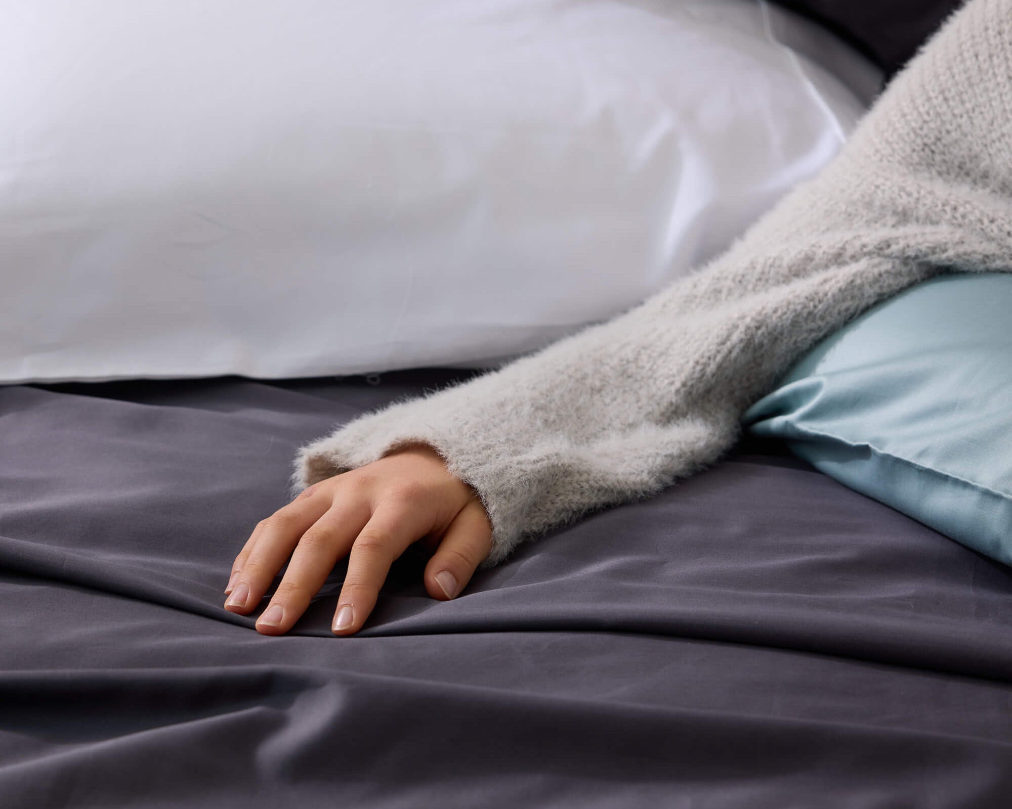 Hand resting on a charcoal Royal Doulton Ceilo sheet with white and sage pillows