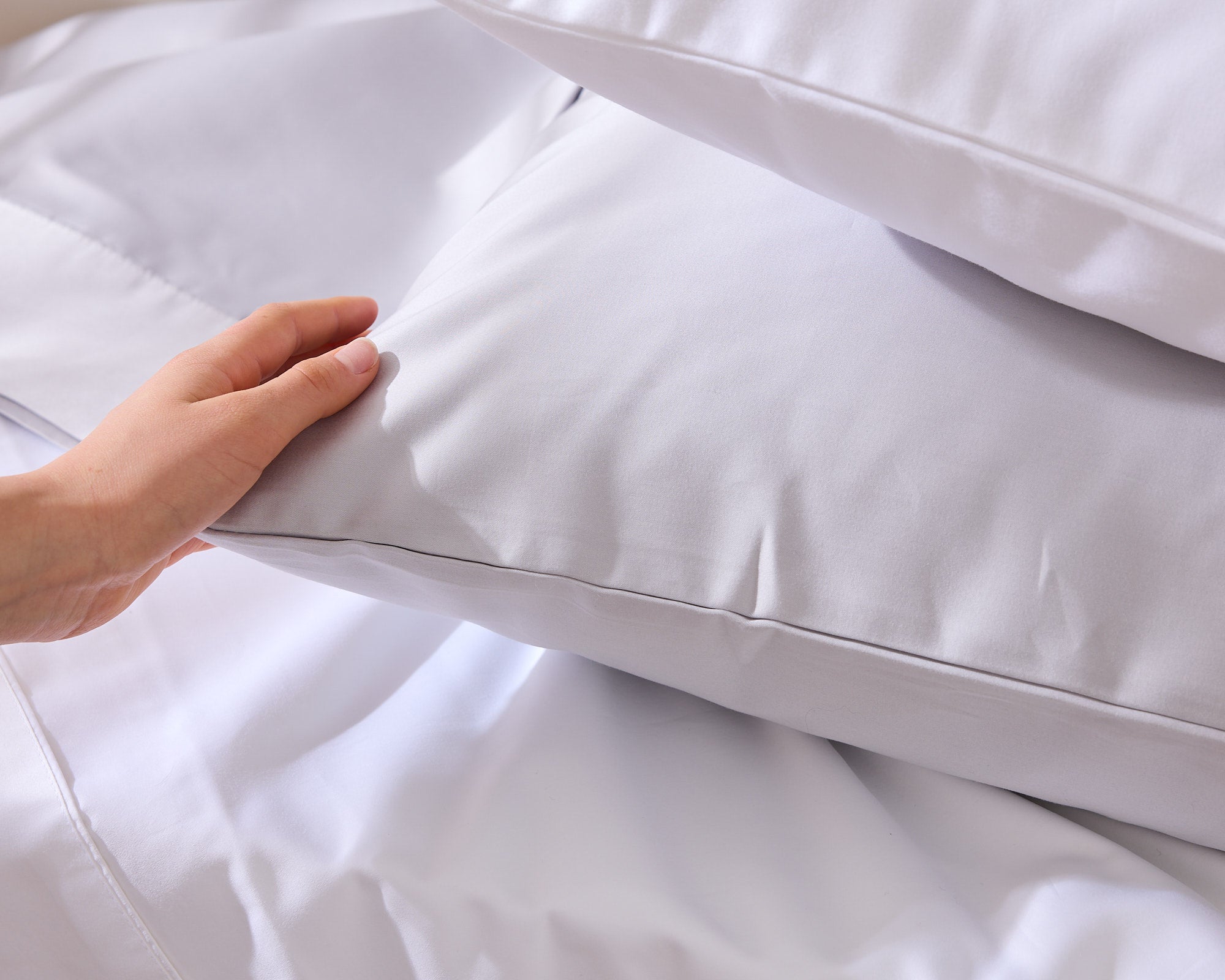Hand smoothing a white Royal Doulton Aria pillowcase on a bed
